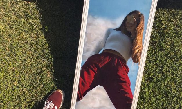 Pantalón rojo y zapatillas reflejados en un espejo sobre el césped.
